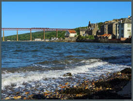 Während unten die Wellen am Ufer von South Queensferry brechen, rollt im Hintergrund ein Triebwagen der Baureihe 170 in luftiger Höhe über die Fifth of Forth-Brücke.