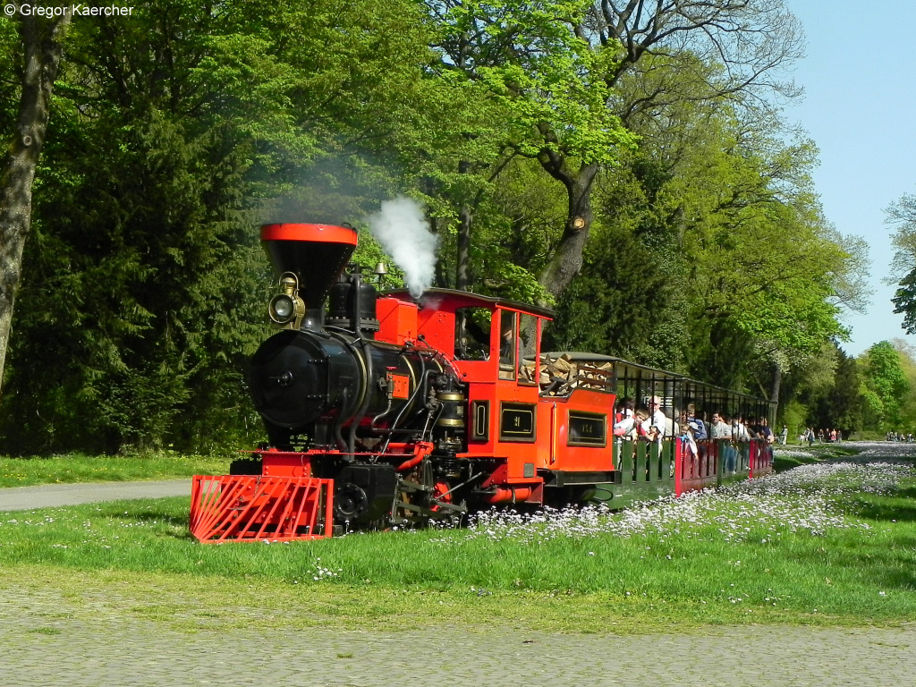 10.04.2011, Schlossgartenbahn Karlsruhe. Die Dampflok 21 Greif mit ihren 4 Wagen, hier im stlichen Schlossgarten unweit der Uni Karlsruhe. Der Zug nhert sich einen Bahnbergang und der Lokfhrer setzt gerade zum Pfiff an.