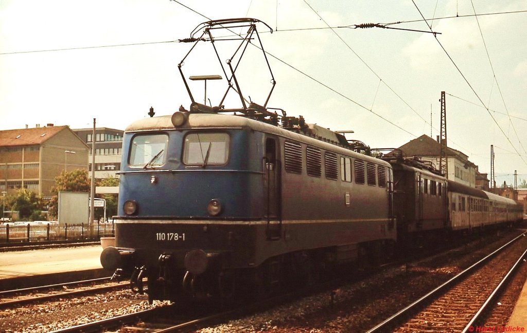 110 178-1 und eine abgebügelte 144 vor einem Nahverkehrzug im Mai 1978 im Bahnhof Reutlingen. Zwar fast eine Gegenlichtaufnahme, aber die Lok befindet sich noch weitgehend im Originalzustand ohne DB-Logo, dafür hat sie noch die Stirnlampen mit integriertem Rotlicht und eine große Dachleuchte, einen weißen Zierstreifen zwischen Rahmen und Aufbau, Regenrinne, umlaufende Griffstange, Trittrost, Lamellen-Lüftungsgitter und Maschinenraumfenster zum Öffnen.   