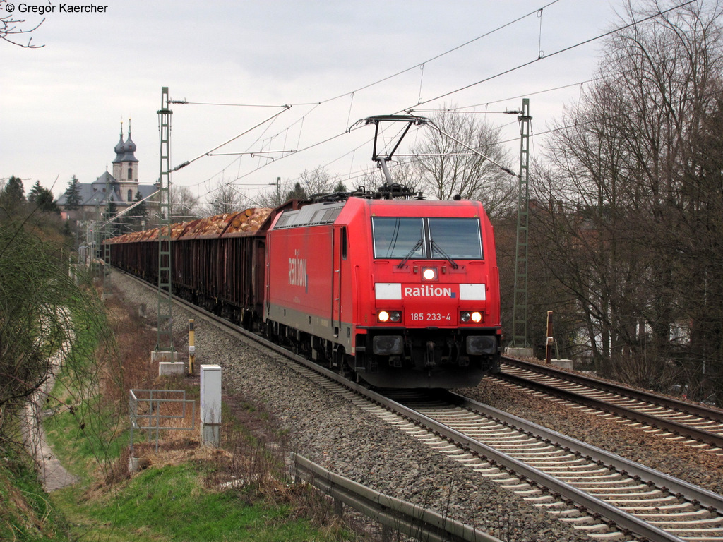 11.03.2011: Die 185 233-4 mit einem Holzzug Richtung Sden bei Bruchsal-Schlachthof. Im Hintergrund die St. Peterkirche von Bruchsal. Ein Gru auch an den TF.