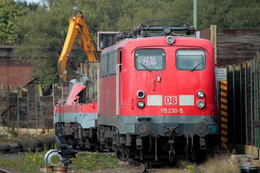 115 230-5 steht am 23.09.2011 noch relativ unversehrt beim Schrottverwerter Theo Steil in Eschweiler-Aue. Die dahinterstehende 115 148-9 ist schon zum groen Teil demontiert. Gerne wrde ich auf dem ausgebauten Tf-Sitz der am unteren linken Bildrand steht Platz nehmen wenn die Lok`s mit Bagger und Schneidbrenner zerlegt werden, aber leider darf man nicht auf das Gelnde der Firma. So bleibt einem nichts anderes brig das interessanten Treiben auf dem Zerlegegleis von der Strasse aus durch den Zaun zu beobachten.