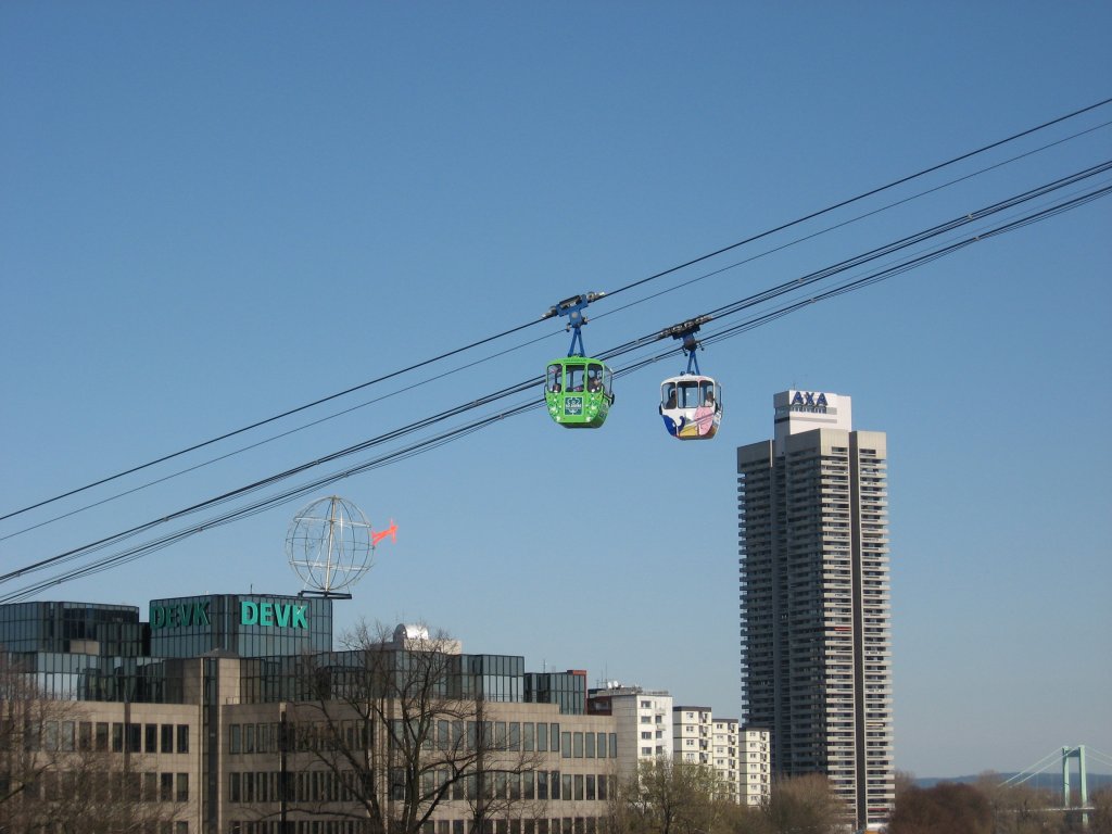 2 Seilbahnen der Rheinseilbahn Kn begegnen sich am 06. April 2010 vor der Kulisse des Hochhauses der AXA-Versicherung und dem Gebude der DEVK Versicherungen. Auf dem Dach der DEVK ist eine Weltkugel mit einem roten Menschen, die von dem Knstler H. A. Schult ist. Die Kugel war vorher auf dem Brckenpfeiler der Severinsbrck gewesen.
