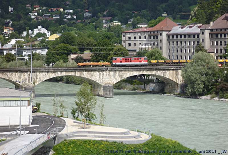 2143-037 passiert mit endlosem Bauzug mit Schotterkbeln die Innbrcke nach Mhlau. Zwei Kilometer weiter stlich, auf Rum zu, ist man eifrig damit beschftigt, die Gleise neu zu legen. Ende Juni 2011 kHds