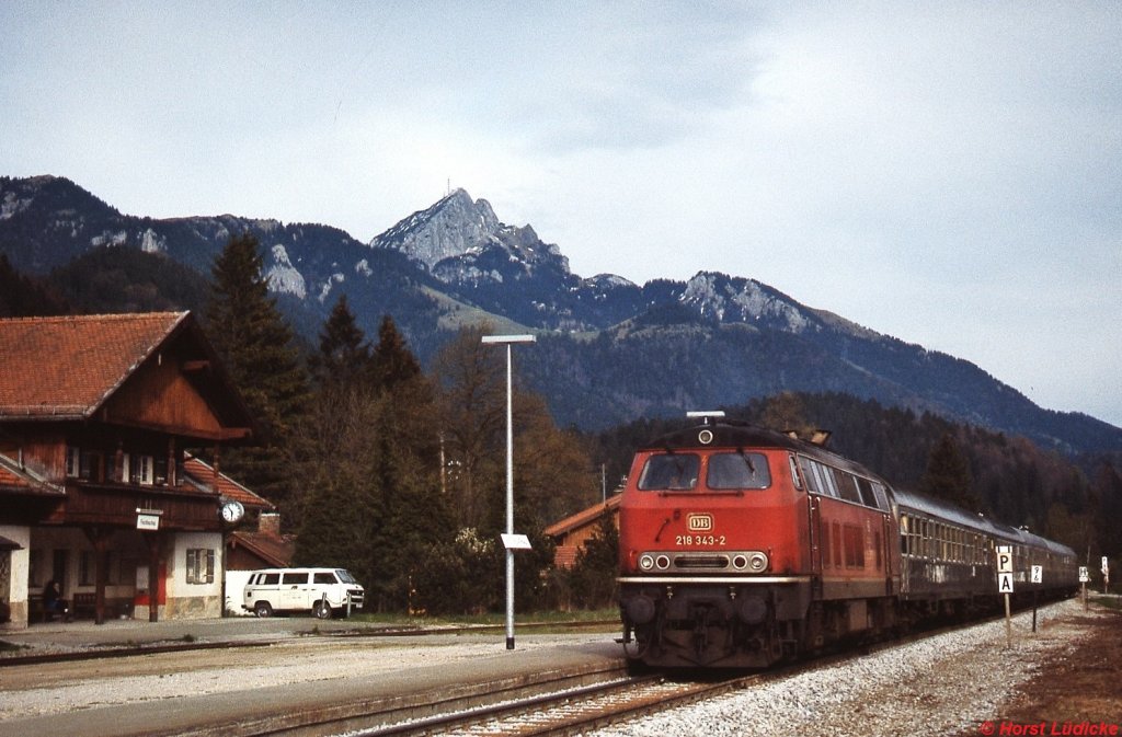 218 343-2 fährt im Dezember 1985 mit einem Zug von Bayrischzell nach München in Fischbachau ein. Zugkreuzungen waren zu diesem Zeitpunkt nicht mehr möglich, es existierte nur noch das vor dem Empfangsgebäude sichtbare Abstellgleis. Der Bahnhof war schon längst geschlossen, aber noch DB-Eigentum. Heute befindet sich das Gebäude, schön renoviert, in Privatbesitz.