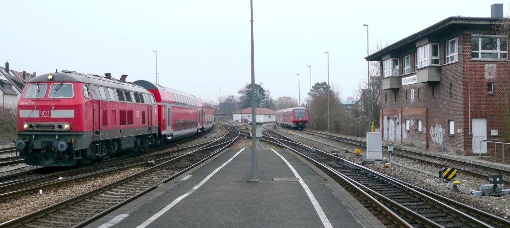 218 431 fhrt am 7.4.13 mit einem RE aus Ulm in Friedrichshafen Stadt ein. Rechts wartet ein VT 611 vor den zum Hafenbahnhof fhrenden Gleisen. 