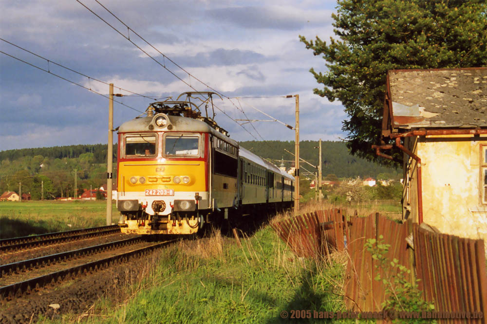 242 203 kommt mit einem Personenzug zwischen Kynsperk und Cheb bei Chotikov am 10.05.05 an einem abgeirtschafteten Bahnwrterhaus vorbei.