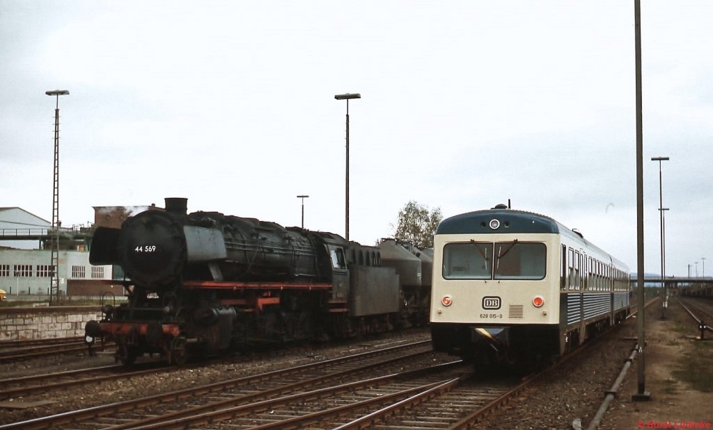 628 015-0 verläßt im April 1976 den Bahnhof Herzberg. Die vor einem Güterzug auf die Ausfahrt in Richtung Northeim wartende  44 569  war zu diesem Zeitpunkt längst computergerecht in 044 569-2 umgezeichnet. Eisenbahnfreunde hatten eine Klebefolie mit der ursprünglichen Loknummer an der Rauchkammer angebracht.