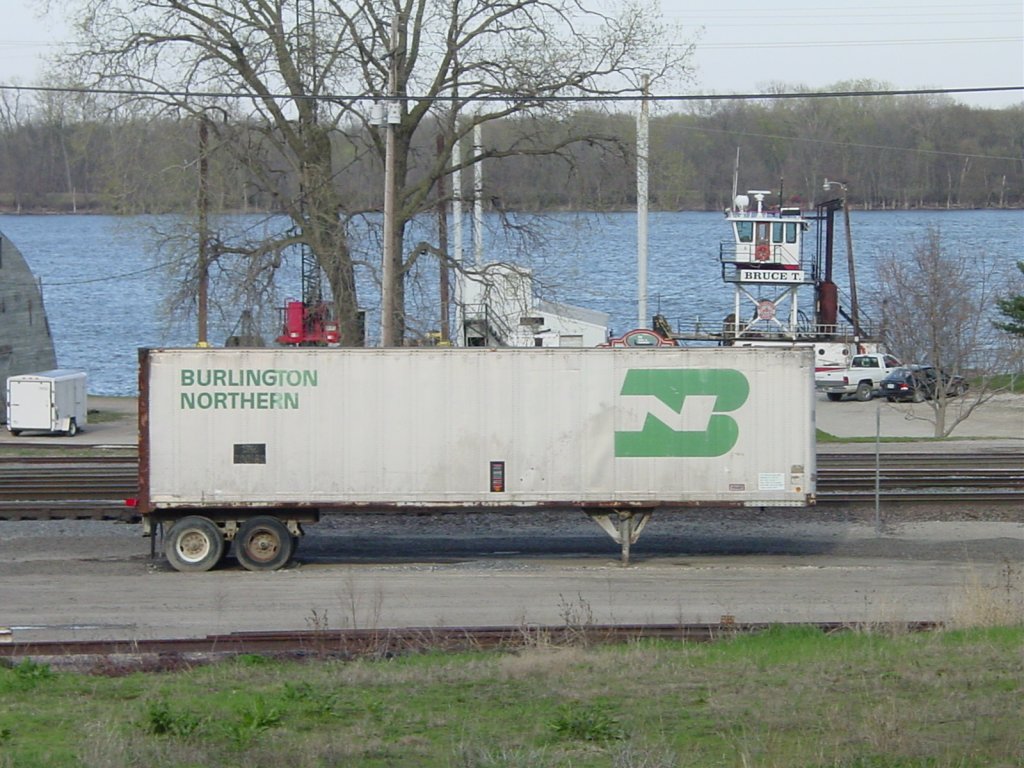 A 40 foot long aluminum semi trailer with the pre merger paint scheme of Burlington Northern sits in the rail yard of his name sake, Burlington. The Mississippi River is in the background.