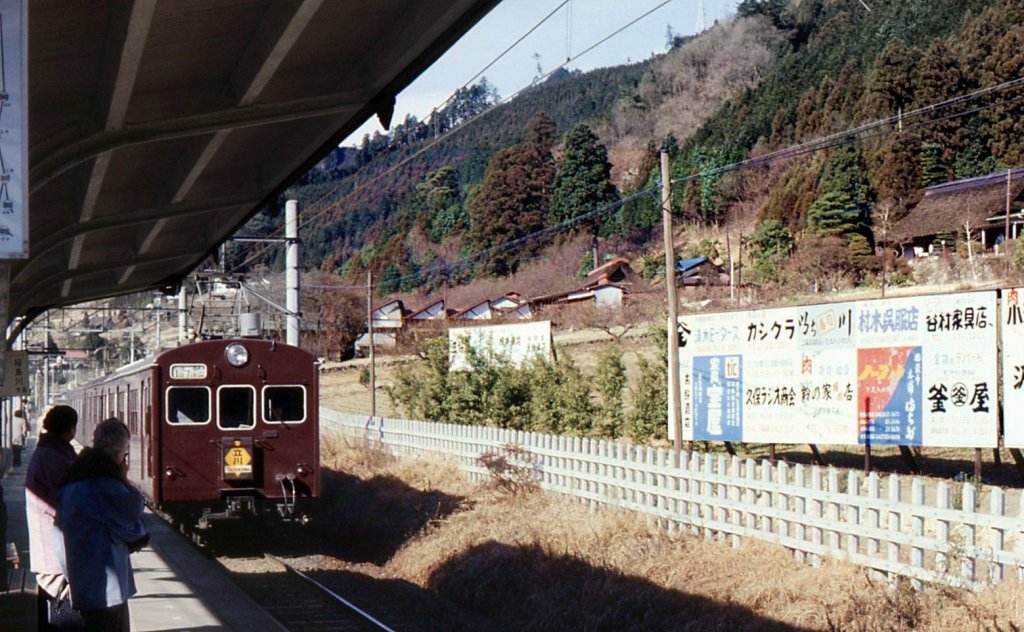 Altbautriebwagen ehemalige Staatsbahn JNR Serie 72: Noch tragen viele Frauen traditionell japanische Kleidung, noch sind Bauernhäuser vielfach strohbedeckt. Einfahrt des Triebwagens KUMOHA 73 137 mit Neubau-Wagenkasten von 1960 in Sawai im gebirgigen Hinterland von Tokyo, 22.Januar 1977. 