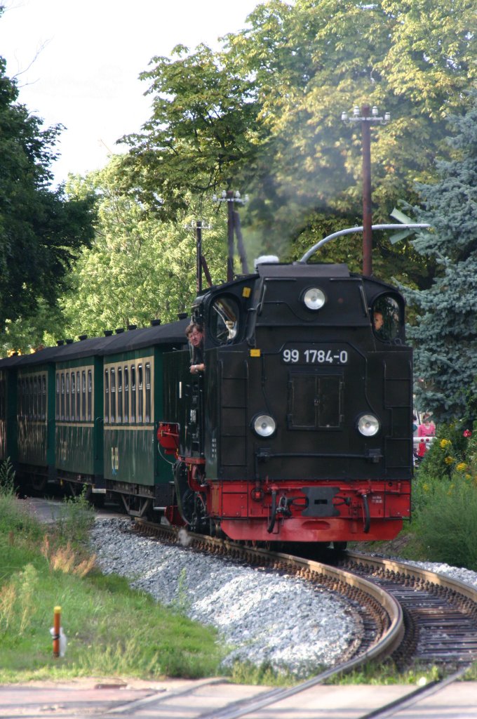 Am 19.08.2010 zieht 99 1784 - 0 den vorletzten Zug  von Binz nach Ghren gegen 18:36 Uhr , die Bahn kreuzt hier in Baabe die Strandstrae, eine schne Promenade, die geradewegs zum Ostseestrand fhrt. 