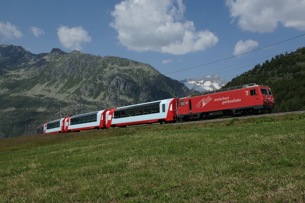 Am 27.7.12 zieht die HGe 4/4 II 102 den Glacier-Express 902 von Andermatt Richtung Disentis, hier bei Ntschen.