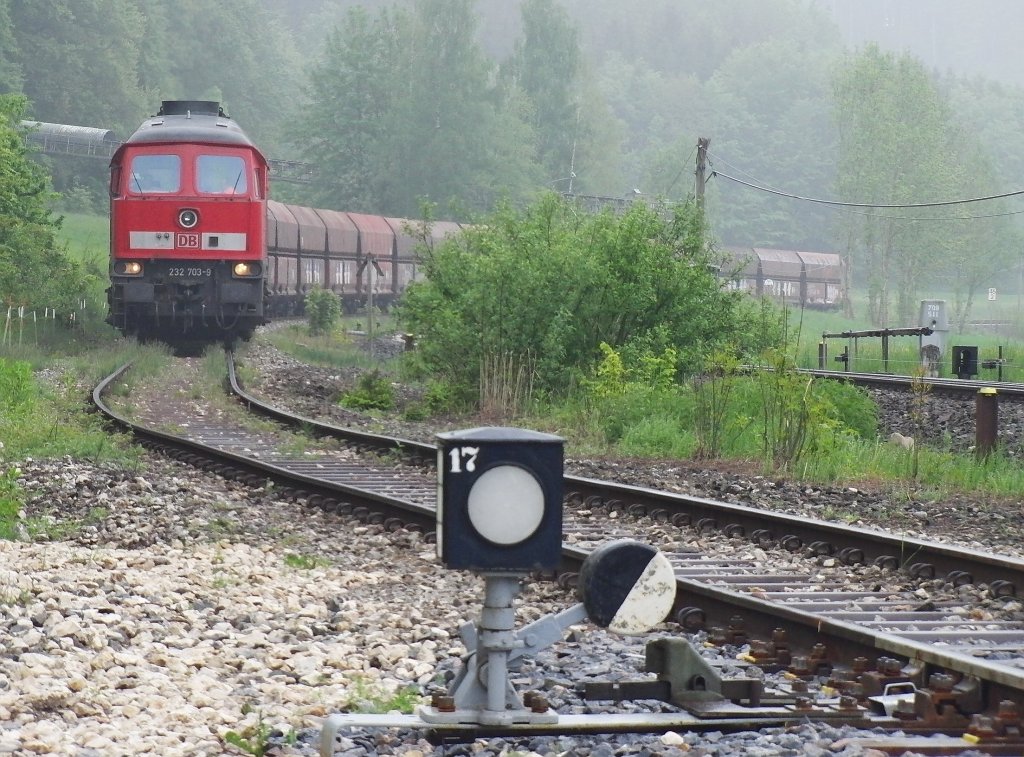 Am nebligen Morgen des 17.05.2013 zieht 232 703-9 auf dem Ladegleis in Roßberg Wagen für Wagen vom Typ Falns weiter, damit diese nacheinander mit Kies befüllt werden können. Links im Hintergrund ist ein Teil der Förderanlage zu sehen, die den Kies vom nahegelegenen Kieswerk zu den Wagen befördert.