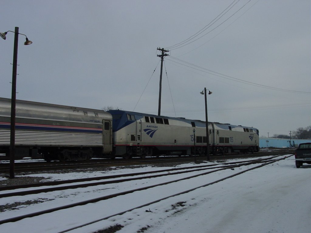 Amtrak 185 & 158 wait patiently on a snowy December day for eastbound passengers to load at Burlington, Iowa. In this very site on the closest track to the right is the same track where the old Injun Joe Zephyr was backed into the depot for its southbound trek to St. Louis, Missouri half-a-century ago. Train is pointing south now, and in less than one mile will be crossing the Mississippi River.