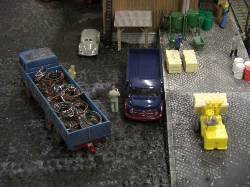 An der Laderampe am Gterschuppen stehen LKW Fahrer Klaus und Karl-Heinz und warte auf die Be- bzw. Entladung.
Whrend Klaus gestern erst seinen neuen Rundhauber bekommen hat, ist der LKW von Karl-Heinz schon ziemlich mitgenommen.
Im Hintergrund steht der neue Brezel-Kfer des Verlademeisters.