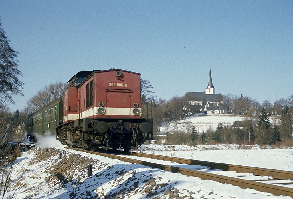 Aus dem Dia-Archiv: 202 806 + RB8659 unterwegs auf der seit Sommer 1996 stillgelegten Strecke Schleiz - Saalburg, mit der Schleizer Bergkirche im Hintergrund. Der von Saalburg kommende Zug wird wenig spter den Hp Schleiz West erreichen. (07.02.1996)