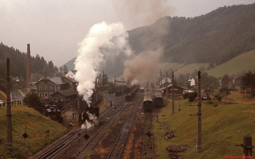 Bahnhof Vordernberg im August 1975: Während im Vordergrund eine 97 rangiert, wartet im Bahnhof ein Leerzug mit einer 197 als Zuglok auf die Abfahrt in Richtung Präbichl. Links neben ihr sind auf dem Heizhausgelände einige bereits abgestellte Lokomotiven zu erkennen. Gut sichtbar ist im Vordergrund der Beginn des Zahnstangenabschnittes. 