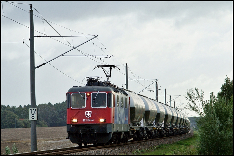 Bei diffusem Gegenlicht und Nieselregen ist Re 421 375-7 mit dem MWB-Zementer von Sassnitz-Mukran nach Itzehoe am 18.09.2010 kurz vor Kummerow unterwegs.