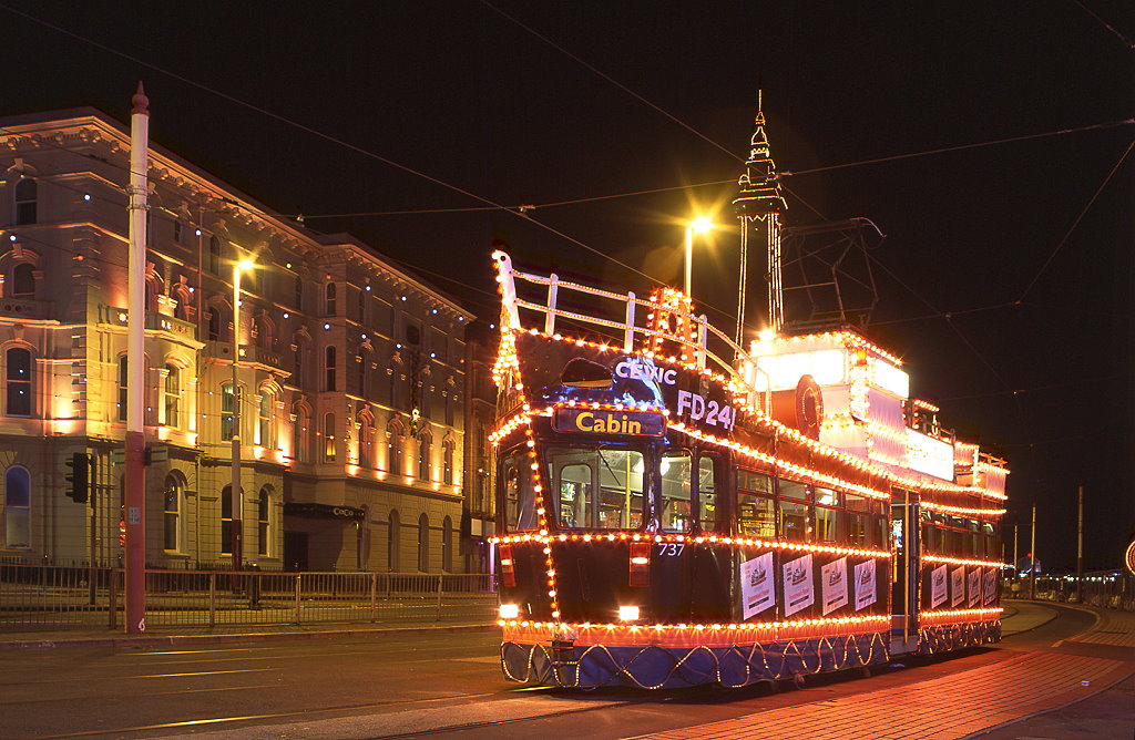Blackpool 737, North Pier, 05.09.2010.



Blackpool Tw 737 wartet an der Haltestelle North Pier auf Passagiere zur Rundfahrt entlang der beleuchteten Hauptstraßen während der Blackpool Illuminations, 05.09.2010. Die allabendlichen  Lichtspiele  werden 2011 vom 02.September bis zum 06.November stattfinden. Zur Dämmerung werden unzähige Laternen und beleuchtete Kulissen auf einer Länge von mehreren Kilometern entlang der Straßenbahnlinie eingeschaltet. Auf der parallelen Straße geniessen die Autofahrer das Spektakel in endlosen Staus, die Straßenbahn beteiligt sich mit drei beleuchteten Themenwagen. Wagen 737 wird von einem Hersteller von Mentholpastillen aus dem nahegelegenen Fleetwood (nördlicher Endpunkt der Straßenbahn) gesponsort.