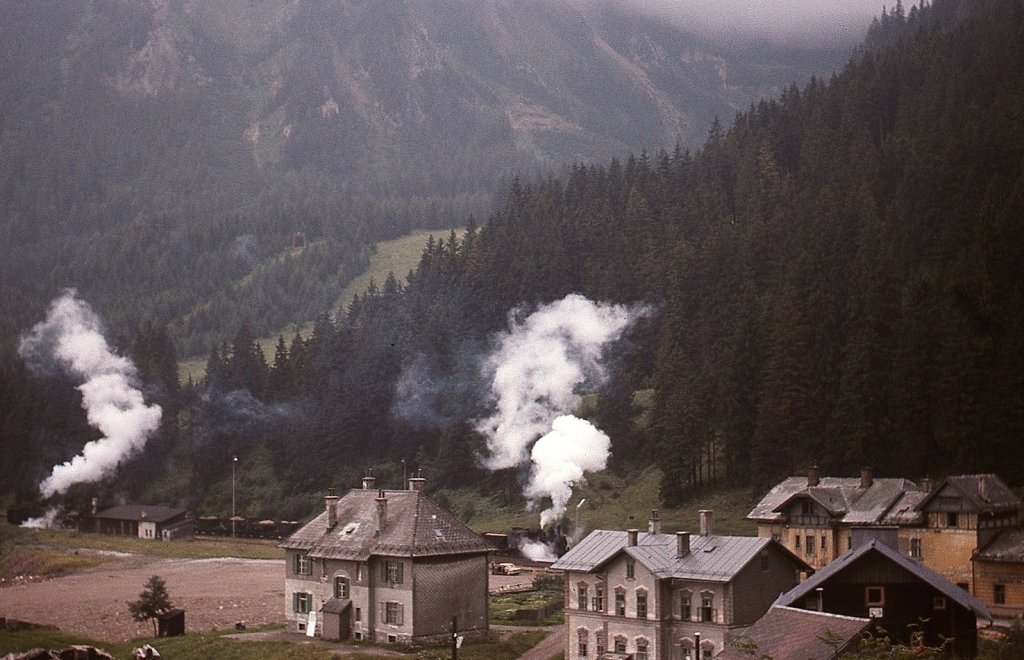 Blick von der Präbichl-Bundesstraße auf den Bahnhof Präbichl, den gerade ein von zwei Lokomotiven der Reihe 97 beförderter Erzzug in Richtung Vordernberg verläßt (16.08.1975)