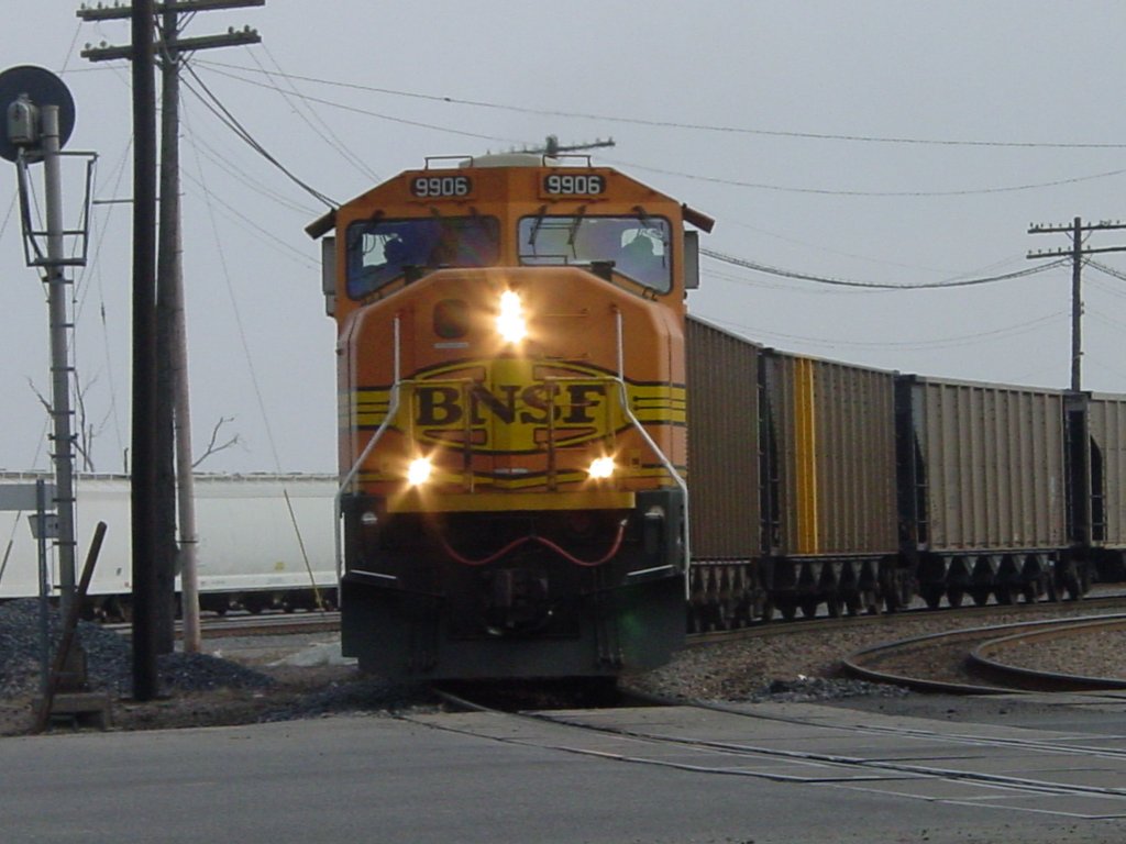BNSF 9906 pulls an empty coal train through the Burlington, Iowa yard and is now about to cross Main Street. Both engineer and conductor are visible as the lower ditch lights are alternating flashing while the horn sounds.