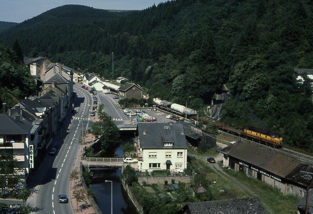 CFL 1814 ist bei Clervaux in Richtung Luxembourg unterwegs, 19.08.1989. Heute verdeckt eine berdimensionale Straenbrcke das Bahnhofsgebude, dem Satellitenbild nach ist das Areal zwischen Fluss und BAhntrasse bis auf das Haus mit der eigenen Brcke eingeebnet.