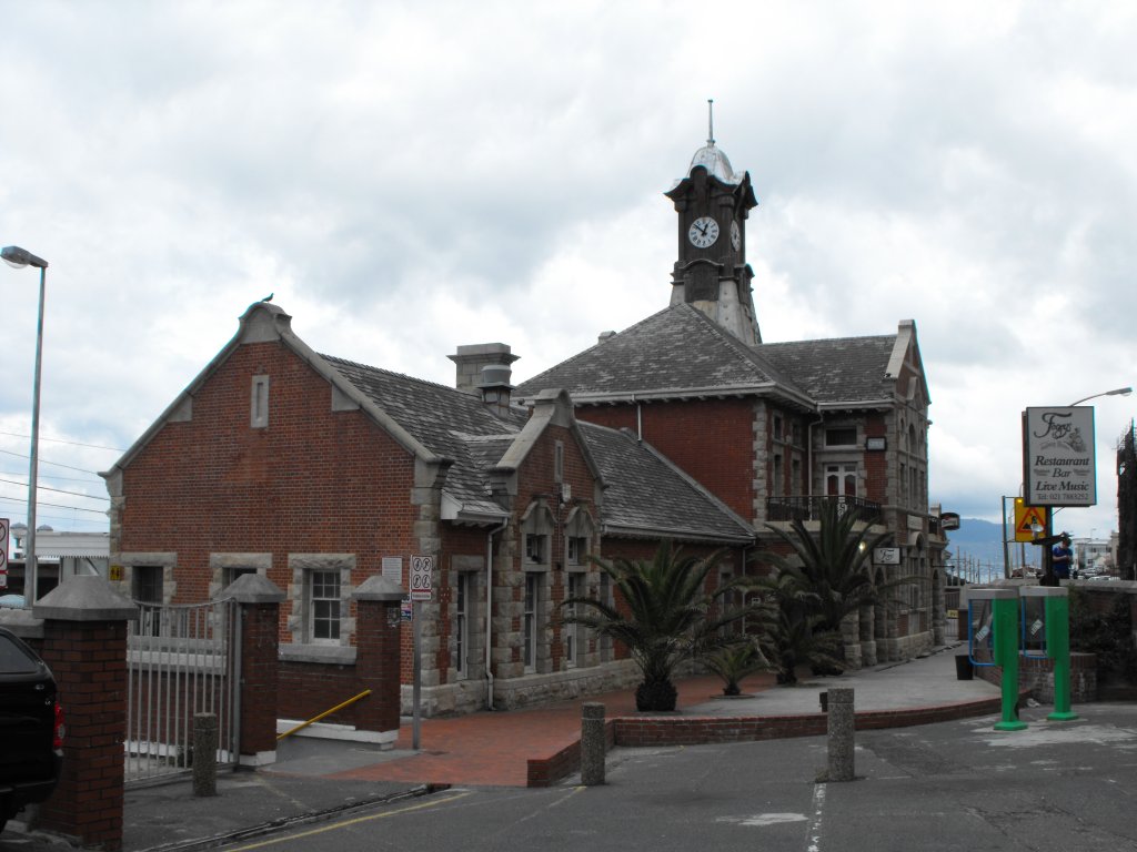 Das verwinkelte und verspielte Bahnhofsgebaeude von Muizenberg steht unmittelbar am Ufer der False Bay. Es steht unter Denkmalschutz, leidet jedoch an Verfallserscheinungen und ist bedraengt durch die Durchgangsstrasse. Aufgenommen von Norden. 20.11.2010