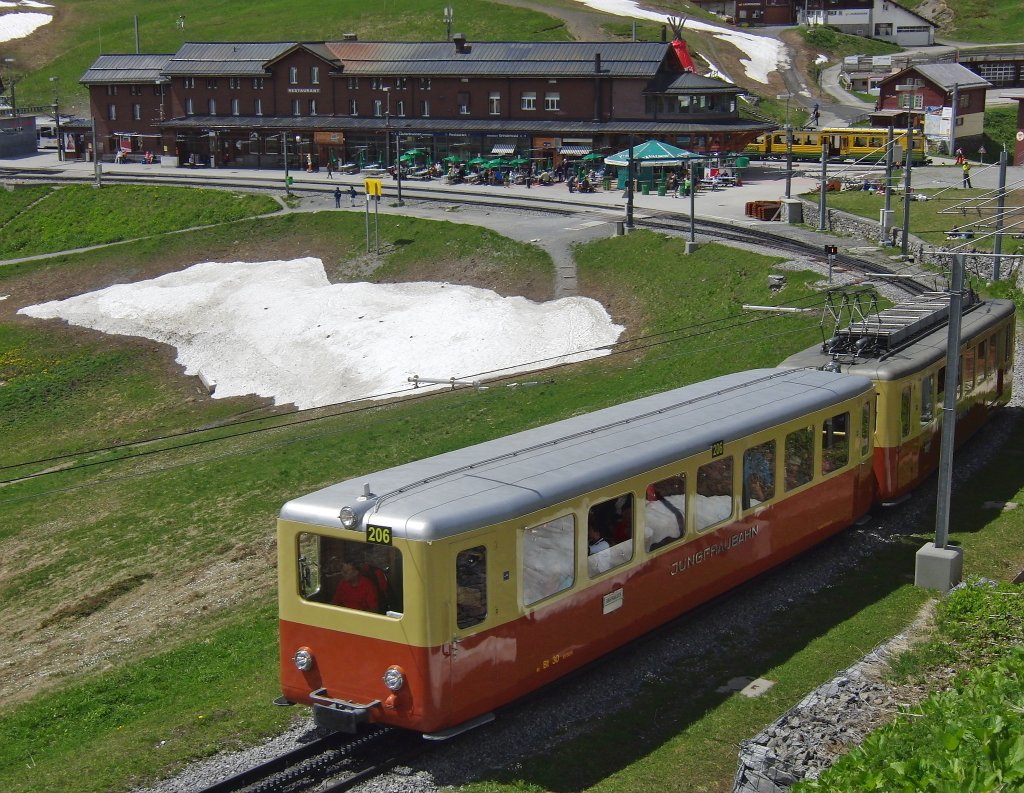 Der 1961 in Betrieb genommene Triebwagen 206 der Jungfraubahn kurz nach dem Start im Bahnhof Kleine Scheidegg (15.06.2013). Rechts hinter dem Gebude ist ein Teil des gelb-grnen Triebwagens der Wengernalpbahn zu sehen, mit der die Gste von Lauterbrunnen aus anreisen.