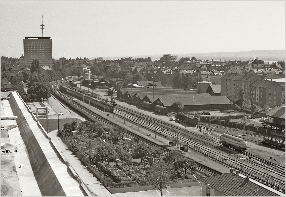 Der Bahnhof Konstanz-Petershausen im September 1970. Auf dem Bahnhof scheint noch viel los zu sein. Ein Eilzug mit V 200, vermutlich von Offenburg, fhrt in das letzte eingleisige Stck zum Hauptbahnhof aus. Die Wgen ein Gemischtwarenladen, mit zwei Umbauvierachsern. An verschiedenen Orten stehen Gterwagen noch einzeln, beim Tank- und Kohlenlager Ellegast im Hintergrund, die Hallen in der Bildmitte waren das Logistikzentrum vom Sdkurier. Angeschnitten vorne rechts das Empfangsgebude. Von dort war der Zugang zum einzigen Bahnsteig. Selber habe ich damals aber noch nicht den Auslser drcken drfen... Auf hohe Kontraste, hufig im Fotolabor bei sw ausgearbeitet, habe ich zugunsten der Details verzichtet.