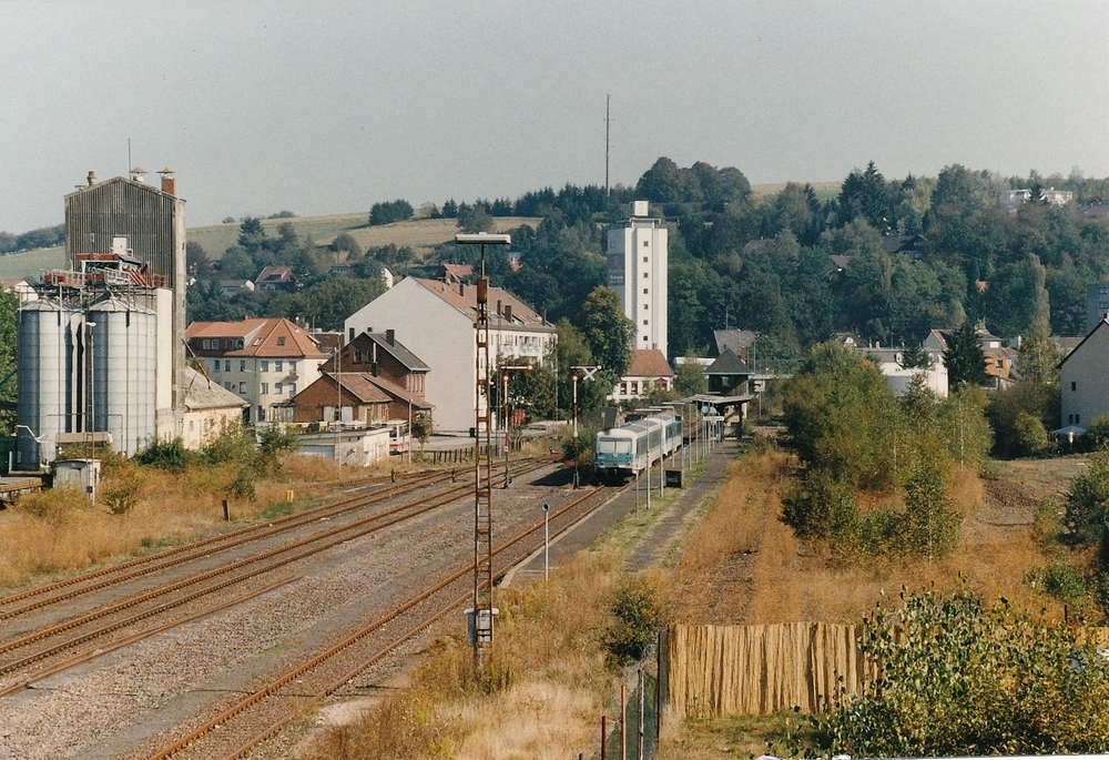 Der Bahnhof Lebach im Jahr 1997 - 

Diesen Blick hat man heute nicht mehr, nicht nur weil der Steg ber die Bahn abgebaut wurde. Auch die Gleisanlagen und Gebude wurden krftig gestutzt.

Das Raiffeisen- und das Bahnhofsgebude sind nicht mehr vorhanden und es gibt nur noch 1 Durchfahrgleis und eine kleine Umfahrung zum kombinierten Bus- und Bahnsteig. Dieser befindet sich dort wo hier noch links zwei Gleise zu sehen sind. Allein das Stellwerk hat die wirren berstanden. Auf der Seite stand noch ein weiterer Bahnsteig mit 2 Gleisen fr die Kllertalbahn (dort wo die Bume schon ein bisschen hher sind)

Im Jahr 2013 soll es wieder verkehrstechnisch noch oben gehen, denn dann soll die Saarbahn ber die reaktivierte Klltalbahntrasse Lebach erreichen.
23.09.1997