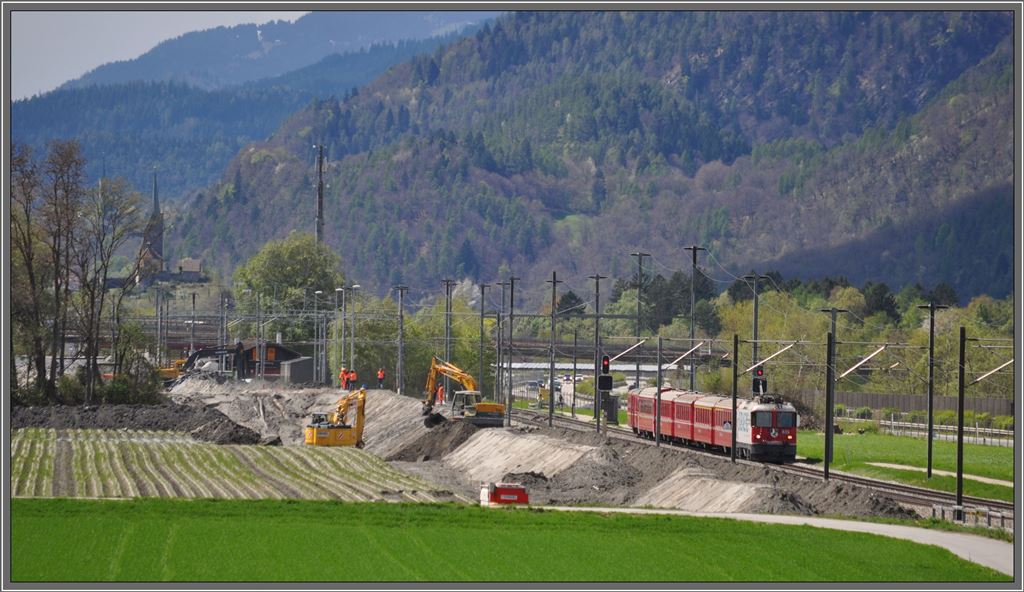 Der RE1249 aus Disentis mit der Ge 4/4 II 616  Filisur  passiert die beiden Bagger, die den Graben ausheben und gleichzeitig den Damm aufschtten. Dahinter erkennt man die Station Felsberg und den Kirchhgel von Domat/Ems. Rfe Pargheratobel.(27.04.2013)