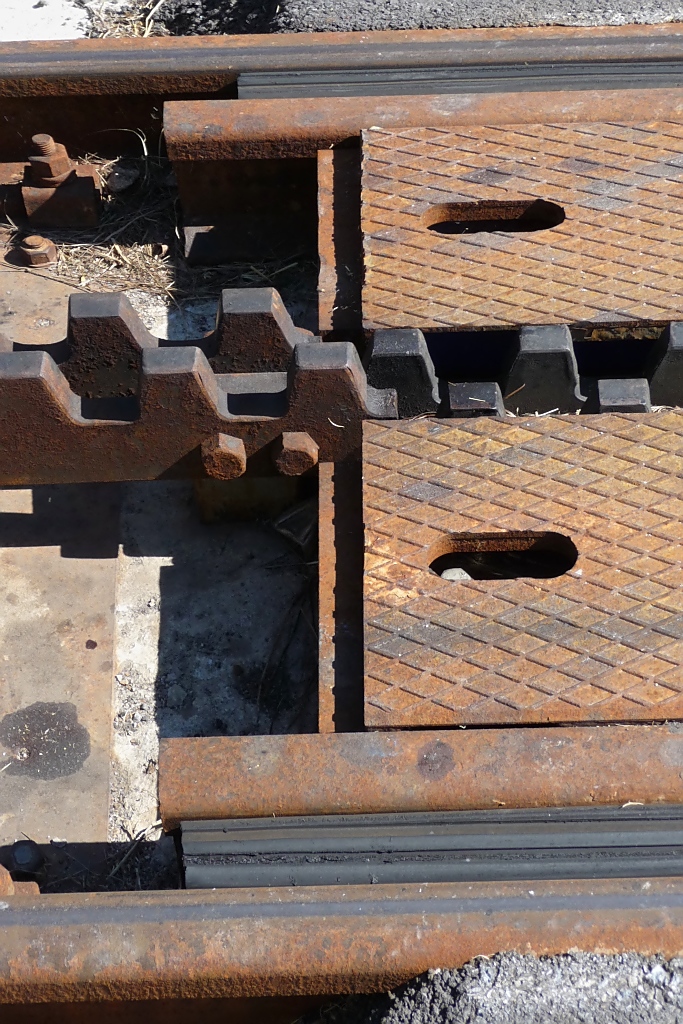 Detailbild (Bahnhofsseite) der versenkbaren Zahnstange auf dem Bahnbergang der DFB ber die Strae von Oberwald nach Obergesteln, 2.10.11. Auch gut zu erkennen ist die Gummi-Abdeckung der Rillenschiene im Straenbereich.