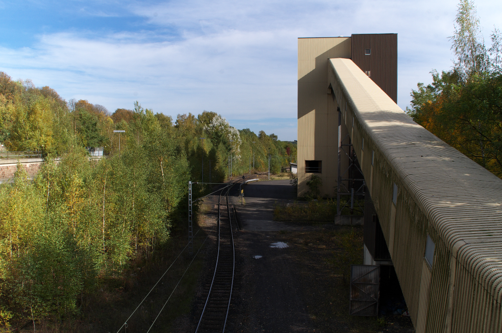Die Anschlubahn zur Grube Gttelborn wurde im Jahr 1891 erffnet und im Jahr 1965 elektrifiziert. Nach Stillegung des Bergwerkes Gttelborn wird die Strecke Merchweiler-Gttelborn noch zur Bedienung des Kraftwerks Weiher genutzt. Links in den Bumen liegen noch vier verwaiste Gleise, die zur Kohleverladung fhrten. 
Frher ging die Strecke etwas gerader unter der Brcke weiter. Durch die Ansiedlung verschiedener Betriebe wurde eine neue Brcke ber die Bahn gebaut, sodass die Trasse den Pfeiler in einer S-Kurve umfahren mu.
Das Gelnde ist grtenteils frei zugnglich, auch Rad- und Wanderwege fhren hindurch und bringen dem Passanten die Industriekultur das Saarkohlenreviers nher.

18.10.2012

