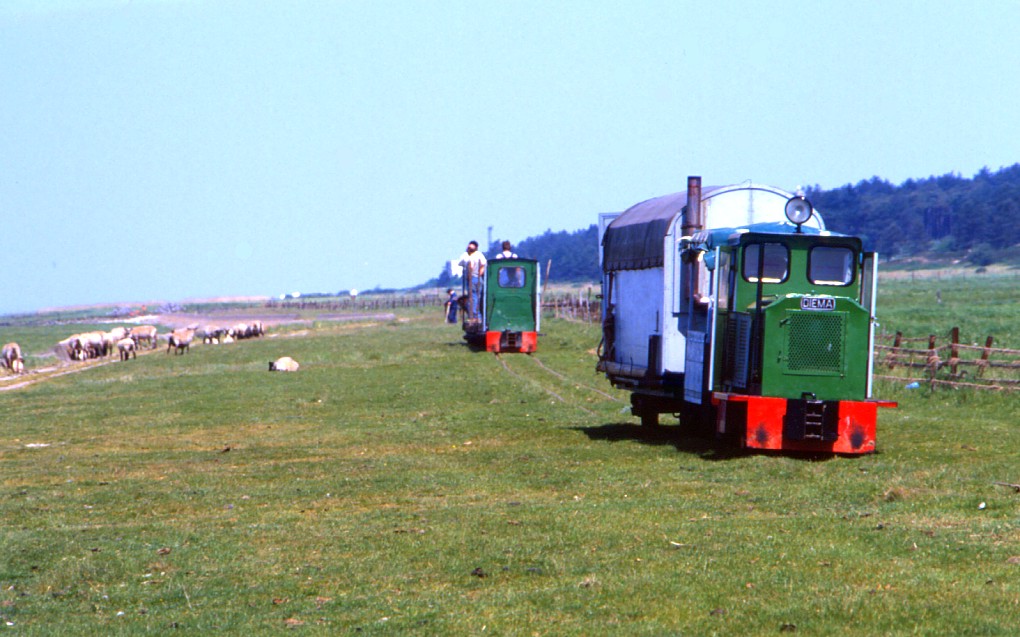 Die Bahn zu den Feldern der Neuland-Gewinnung zwischen Cuxhaven Sahlenburg und Spieka hatte ihren  Betriebsmittelpunkt  in Arensch. Auf dem dortigen Bauhof lagert auch heute noch jede Menge Feldbahn-Material. Aktuell werden nur noch ein paar Hunder Meter Bahn bei Spieka Neufeld betrieben. 
Am 25.05.1989 rckten diese beiden Zge pnktlich zum Kaffee ein - eher eine Ausnahme, denn die Arbeiszeiten in der Neuland-Gewinnung richten sich nicht nur nach Tages-Zeiten sondern auch nach Ge-Zeiten.