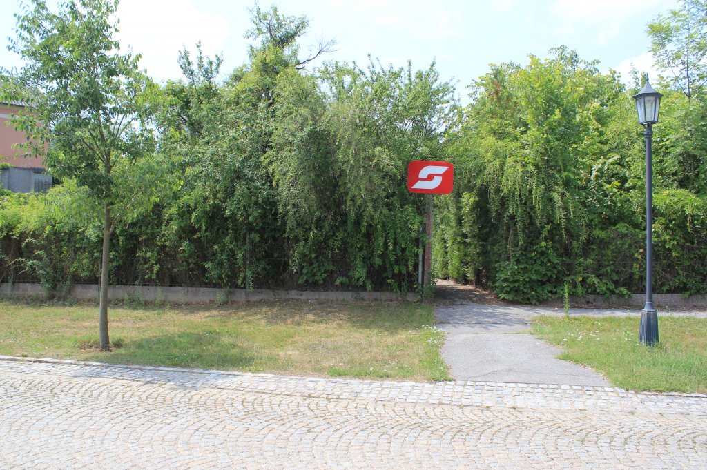 Die Haltestelle in Weikendorf (liegt an der Bahnverbindung Gnserndorf-Marchegg) ist nur durch einen kleinen Zugang von der Strae aus erreichbar. Das BB Schild neben dem Zugang weist den Weg. Links hinten sieht man auch einen Teil des Wartegebudes, Juli 2012