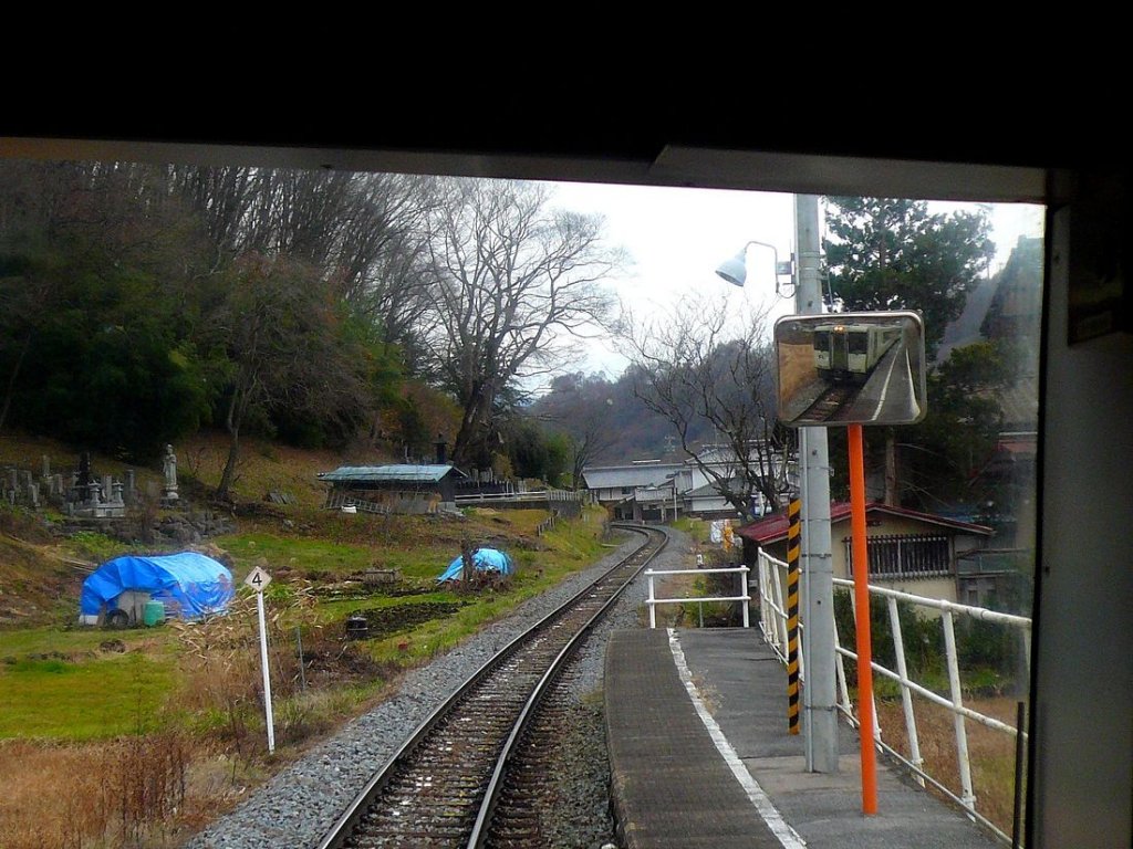 Die KIHA 110 der Koumi-Linie, Japans höchstgelegener Bahnlinie; beim Aufstieg an der Nordseite des Passes. Im Spiegel ist KIHA 110-112 an der Haltestelle Takaiwa sichtbar; links davon am Hang verschiedene Grabanlagen. 24.November 2009. 