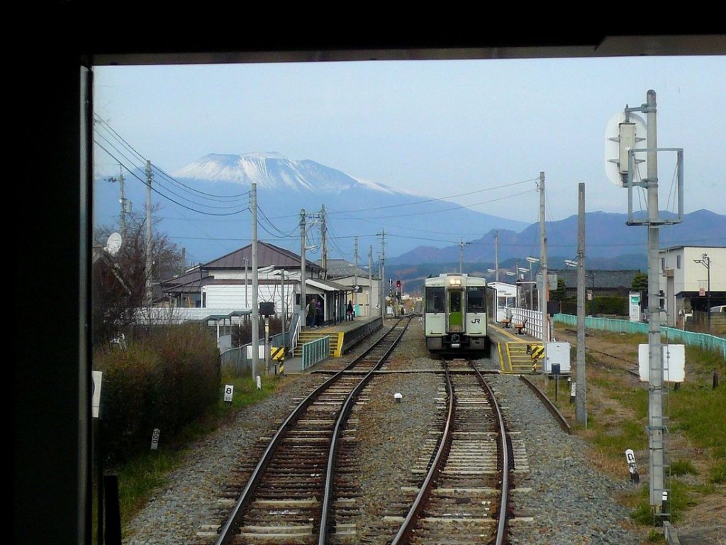 Die Koumi-Linie der JR ist Japans höchstgelegene Bahnstrecke und erreicht 1345 m.ü.M. Sie ist 78,9 km lang, hat 31 Stationen, Steigungen von 33 Promille und führt von Kobuchizawa in der Präfektur Yamanashi steil hinauf ins Hochland von Nagano, wo sie in Komoro endet. Heute wird sie mit den Triebwagentypen KIHA 110/111/112 und den 3 Hybrid-Triebwagen KIHA E200 betrieben. Im Bild wartet vor der Kulisse des aktiven Vulkans Asama-yama die Komposition KIHA 112-111 + KIHA 111-111 in der Station Usuda. 24.November 2009. 