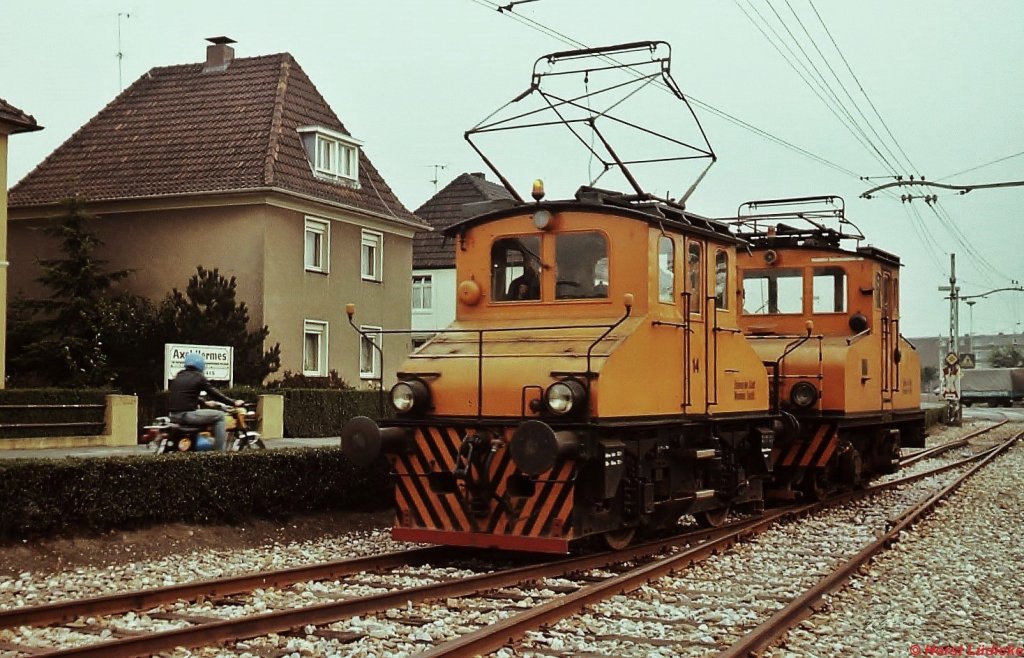 Die Lokomotiven 14 und 15 der Bahnen der Stadt Monheim sind im Sommer 1977 vom Betriebshof aus unterwegs in Richtung Monheim Shell, um einen Kesselzug abzuholen. Damals betrieb die mit 800 V Gleichstrom elektrifizierte Bahn noch das komplette Netz von Leverkusen-Hitdorf bzw. Baumberg durch die Innenstadt von Monheim nach Langenfeld (dort Anschluss an die DB-Strecke Dsseldorf - Kln).  