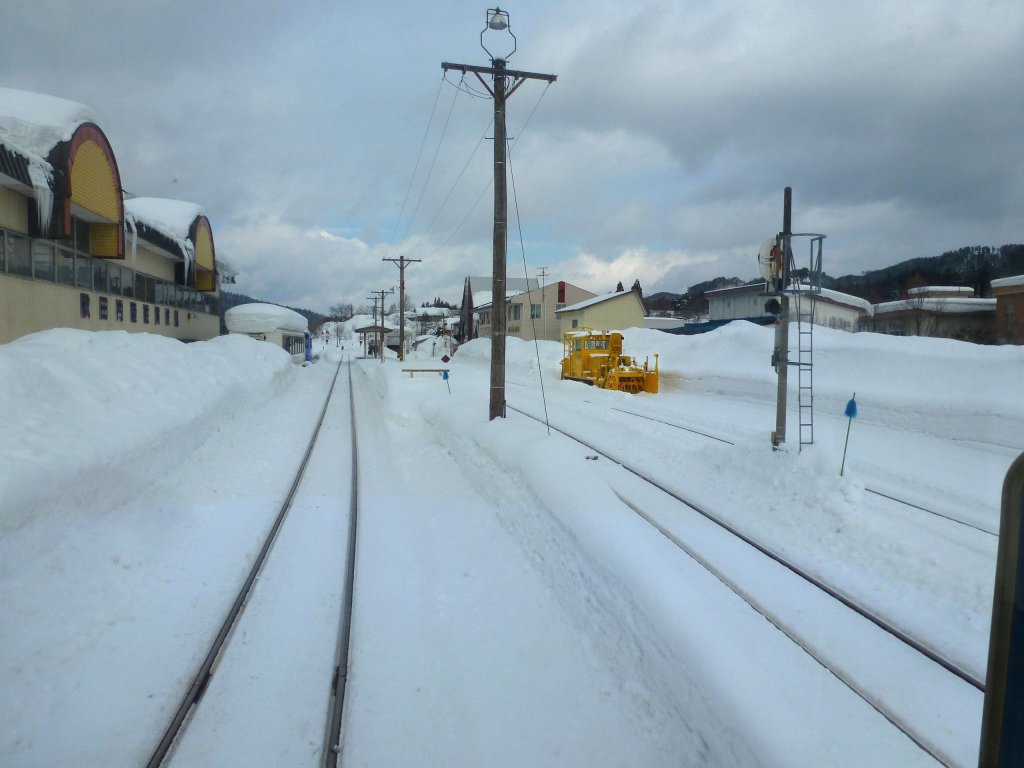 Die Ortschaft Aniai ist das Zentrum der Akita Nairiku-Bahn, mit Depot und Werkstatt. Im Bild: Einfahrt in Aniai, links tief verschneite Wagen, rechts ein Schneerumungsfahrzeug. 14.Februar 2013. 