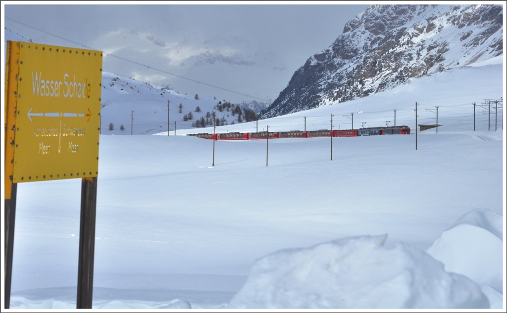 Die Tafel am nrdlichen Ende des Lago Bianco markiert die Wasserscheide zwischen Adria und Schwarzem Meer.Im Hintergrund erscheint der R1625 mit den direkten Bernina-Express-Wagen ab Chur. (22.02.2011)