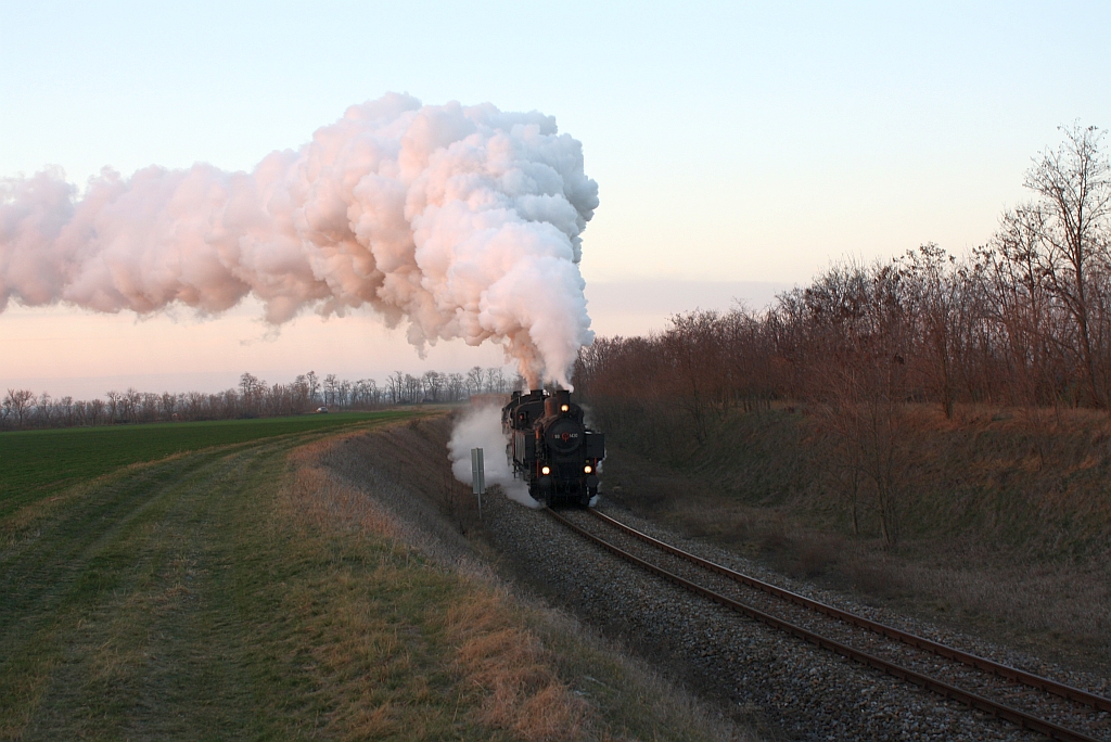 Die tiefstehende Sonne kurz vor ihrem Untergang taucht die Abdampfwolken der NLB 93.1420 und der VdEA 52.4984 in seltsam anmutendes Rosa. Aufnahme vom 09.12.2012 im letztem Bogen vor dem Bf. Hohenau.