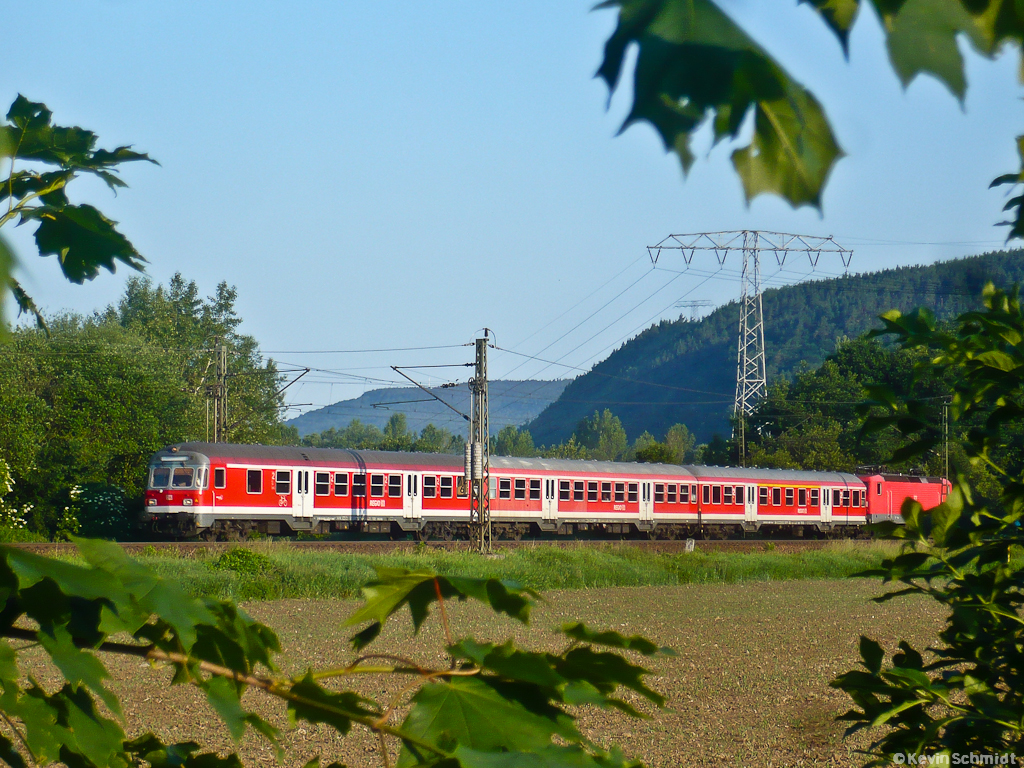 Dieses Bild entstand an einem sonnigen Morgen am Rande von Saalfeld und zeigt die montags bis freitags verkehrende RB von Jena Saalbahnhof nach Bamberg, die hier in Kürze den Bahnhof Saalfeld (Saale) erreichen wird. Dieser Zug fährt planmäßig mit n-Wagen und ist damit unter den auf der <a href= https://www.youtube.com/watch?v=DqaBPmjaGNA >Saalbahn</a> eingesetzten Fahrzeugen eine ganz große Ausnahme. (03.06.2011)
