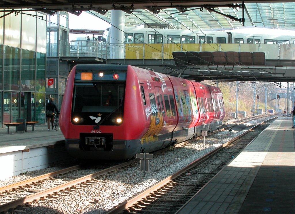 DSB S-Bahn Kopenhagen: S-Bahnlinie F (SH 4702) S-Bf Flintholm am 12. April 2012. - Der Zug fährt in Richtung Ny Ellebjerg. - Über die Brücke hinter dem S-Bahnzug fährt die Kopenhagener Mini-Metro. 