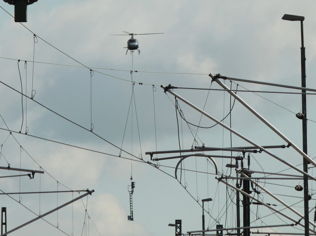 Durch ein Gewirr aus Masten und Leitungen fliegt am 07.08.2011 ein Eurocopter AS350 Ecureuil der Firma KMN Koopmann Helicopters mit einem Signalmast am Haken in Stolberg vom Lagerplatz zum Hbf. Dort wird der Mast von der Bodenmanschaft montiert