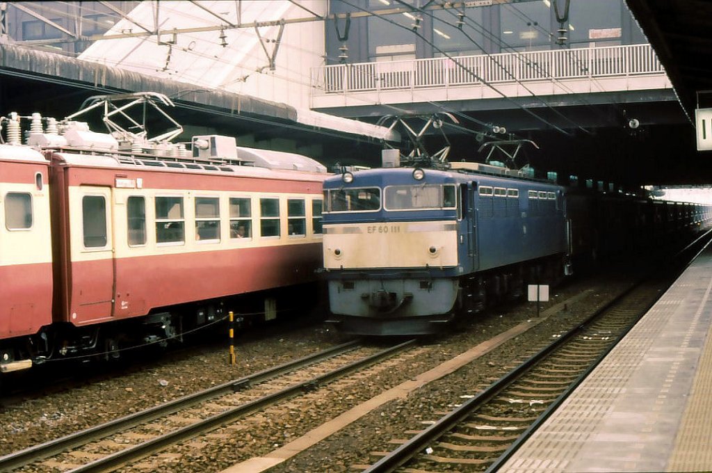 EF60: Lok EF60 111 kommt mit ihrem Güterzug unter dem Bahnhof Ômiya hervor. Daneben steht ein Zweistrom-Schnellzug für einen Dienst nach Nordjapan im damaligen Anstrich rosa/weiss. 8.März 1985. 