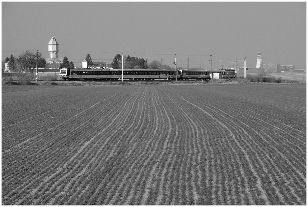 Ein Regionalzug nach Wolfsthal, bestehend aus zwei 4020ern hat soeben Fischamend verlassen und strebt vor dem Wasserturm Fischamend und dem Tower des Flughafens Wien-Schwechat seinem n�chsten Halt in Maria Elend zu, 26.2.2008