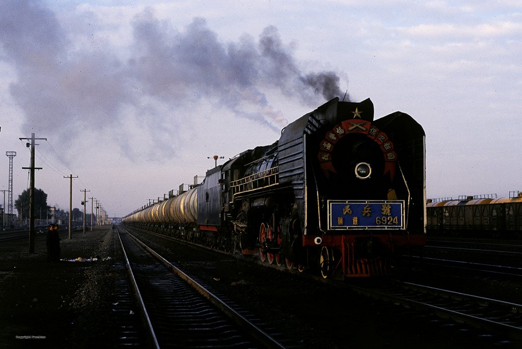 Ein schwerer Ganzzug mit Erdl, wartet auf seinen Abfahrauftrag Richtung Taipingchuang. Das von den lfeldern Daqings und Ranghulu kommende Erdl wird in alle Landsteile geliefert. Bis Anfang des Jahres 2002 oblagen solche Leistungen auf den Strecken von Daan ausgehend, den Loks des Bw Daan Bei. Da es in der Gegend keine groen Steigungen gibt, zogen die zuverlssigen Dampflokomotiven der Baureihe QJ schweren Ganzzge, bis zu 3000t spielend.

China, Okt. 2000 (Diascan)