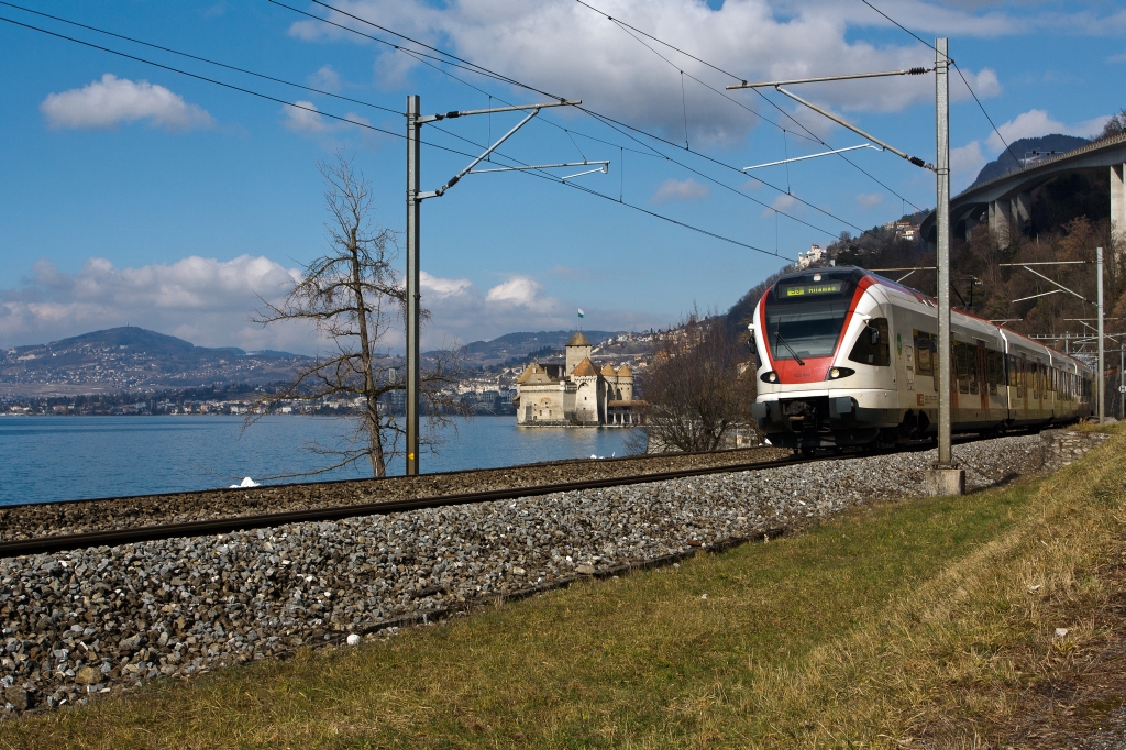 Ein Stadler FLIRT  RABe 523 030 der SBB (RER Vaudois) als S3 (Allaman–Lausanne–Vevey –Montreux–Villeneuve), fhrt am 26.02.2012 bei  Clos du Moulin am Genfersee Richtung Villeneuve, hinten Chteau de Chillon, dahinter Montreux.