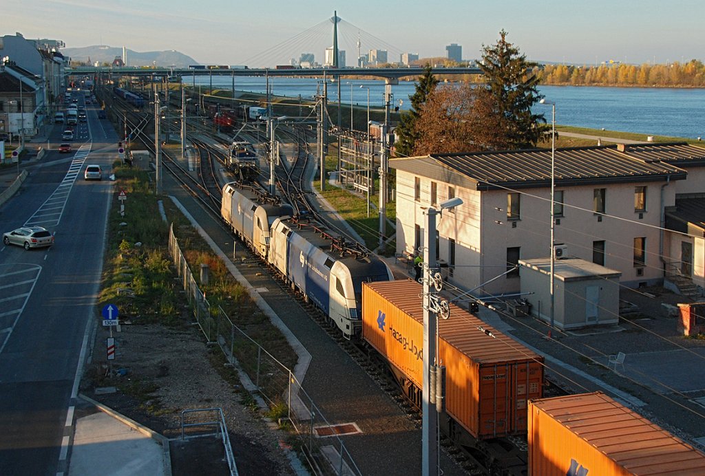 Ein Tandem der Wiener Lokalbahn macht sich mit einem Containerzug auf die Reise. Die Aufnahme entstand im letzten Sonnenlicht des 12.11.2009. Links im HG ist der Leopoldsberg zu erkennen, rechts im HG der Donauturm und die Geb�ude der Wr. UNO City.