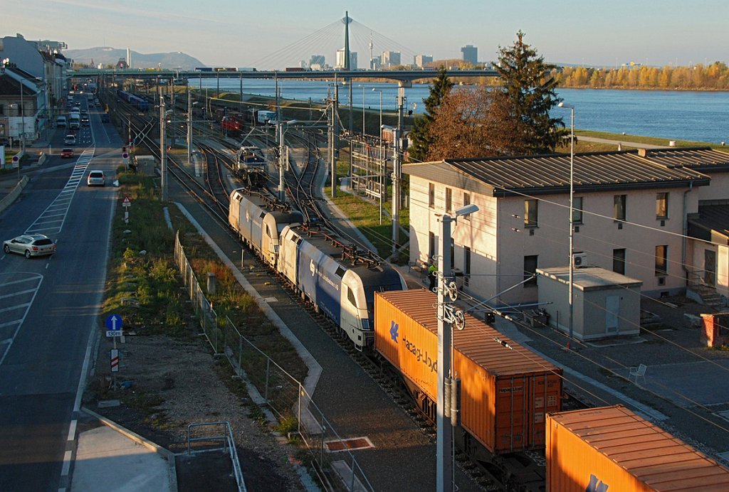 Ein Tandem der Wiener Lokalbahn macht sich mit einem Containerzug auf die Reise. Die Aufnahme entstand im letzten Sonnenlicht des 12.11.2009. Links im HG ist der Leopoldsberg zu erkennen, rechts im HG der Donauturm und die Gebude der Wr. UNO City.
