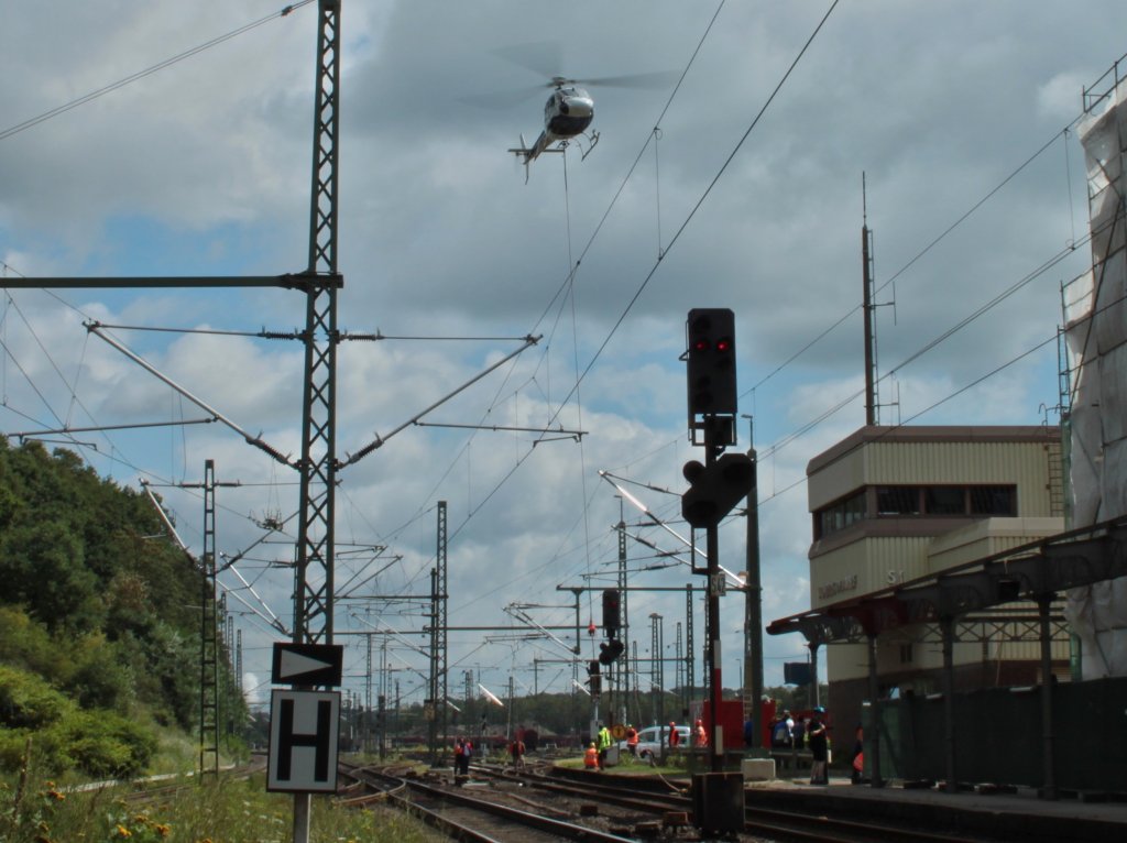 Ein toller Blick vom Bahnsteig am 07.08.2011 in Stolberg Hbf. Ein Eurocopter AS350 Ecureuil der Firma KMN Koopmann Helicopters bringt an einem langen Seil den Signalmast zum Signalfu, wo die Bodenmanschaft den Mast entgegennimmt und mit vier Schrauben sichert. Anschlieend hngt der Hubschrauber den Mast ab und fliegt zum Lagerplatz zurck um den nchsten zu holen. Das ganze dauert ca. 6-8 Minuten pro Signal.